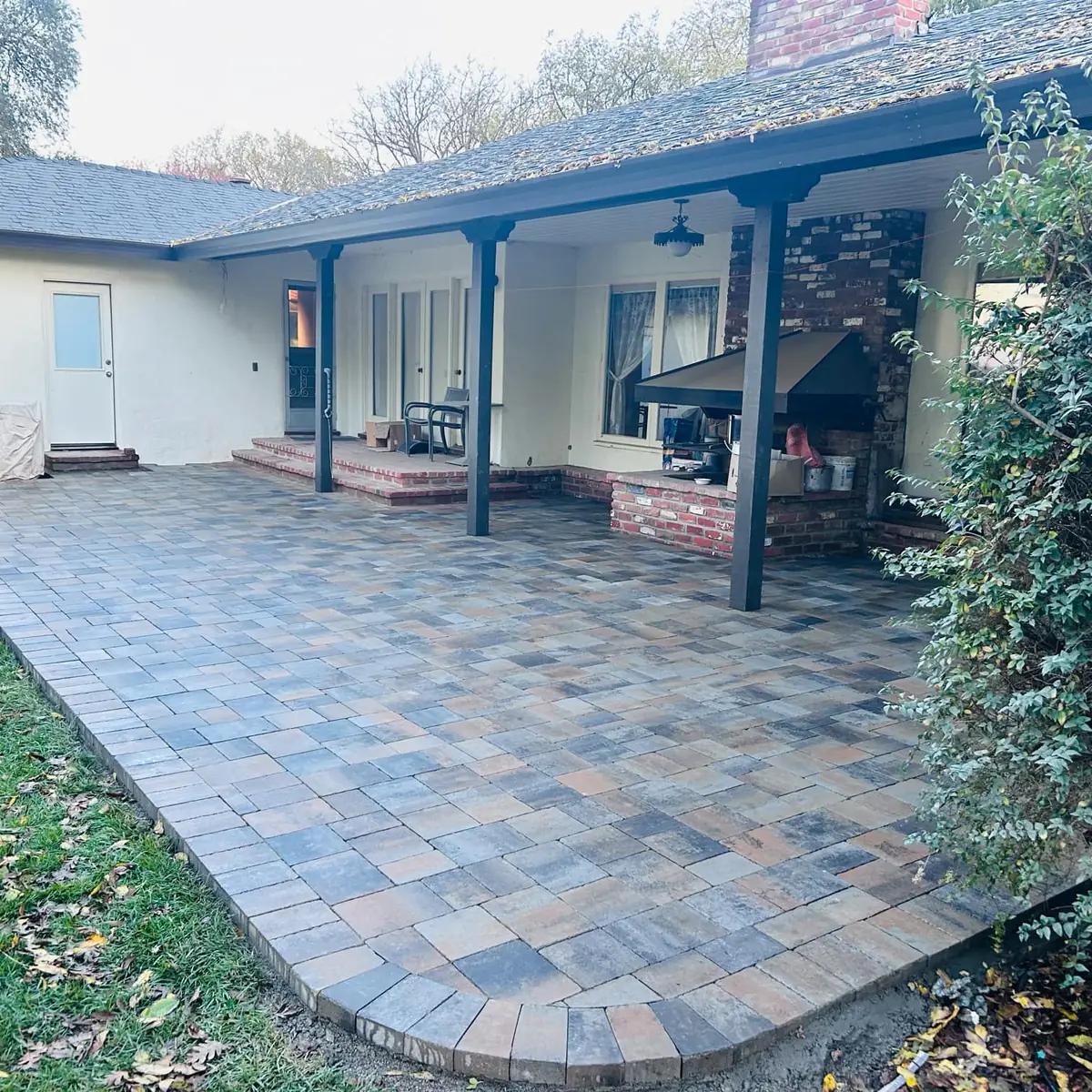 Paver terrace wrapping a Sacramento ranch home with a brick fireplace