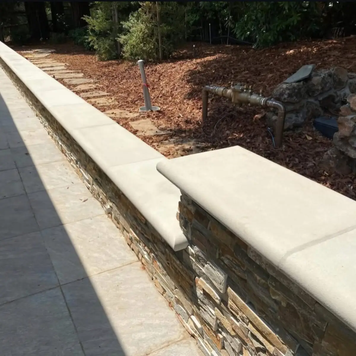 Stone retaining wall with a wide cast cap holding a planted slope