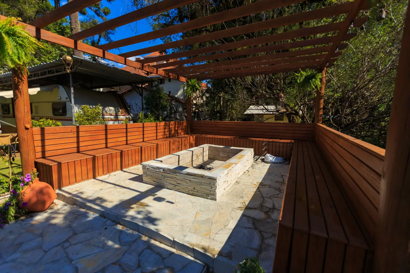 A stone terrace set out under a pergola in a planted garden